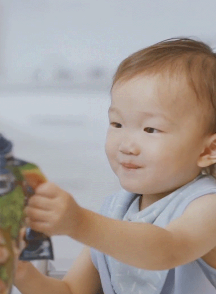 A baby smiles while holding a plant